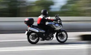 En förare på en pansar mc susar fram på en motorväg, med träd som suddiga gröna streck i bakgrunden.