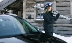 En person med skidor laddar sin elbil vintertid vid en timmerstuga.
