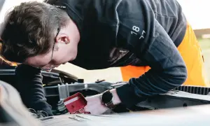 Man med glasögon böjd över bilmotorn, kanske för att fixa det brummande ljudet från bilen.
