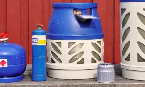 Flera gasflaskor, inklusive en blå gasolflaska och en större vit och blå gasolflaska, står uppradade. Perfekt för din lpg bil.