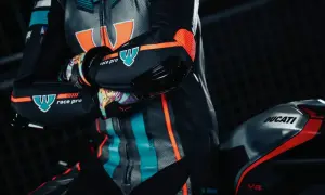 En förare i ett berik skinnställ med orange och turkosa detaljer sitter på en Ducati V4.