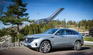 Silver EQC Mercedes står parkerad framför en imponerande hoppbacke i en skogsmiljö.