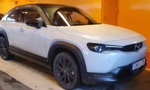 En vit Mazda MX-30 e-Skyactiv med mörka fälgar står parkerad inomhus.