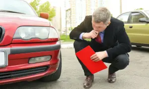 Man i kostym funderar på hur mycket olja rymmer min bil, med en röd pärm i handen vid en röd bil.