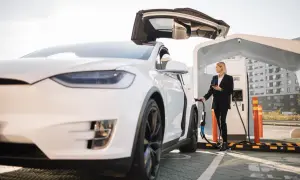Kvinna laddar elbilen gratis vid laddstation. Bilen har uppfällda dörrar.