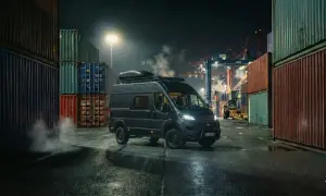 Mörk Fiat Ducato står vid en hamn, omgiven av containrar. Rök stiger från fordonet, vilket antyder ett fiat ducato motor problem.