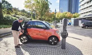Äldre man kopplar laddkabeln till en orange elbil för att ladda elbil 100 procent.