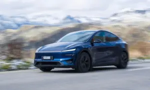 Mörkblå Tesla Model Y Performance kör på en slingrande väg med snöklädda berg i bakgrunden.