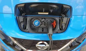 Blue Nissan Leaf with charging port open and cable plugged in.