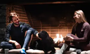 Ett par myser framför brasan med sin hund. Mannen har på sig ett par bekväma underställ byxor.