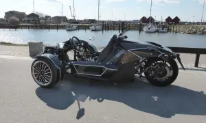 Svart, futuristisk motorcykel på b-kort står vid en hamn med segelbåtar.