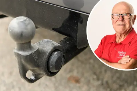 En man i röd tröja från "Tekniker Värld" ler bredvid en avtagbar dragkrok. Viktigt för besiktning.