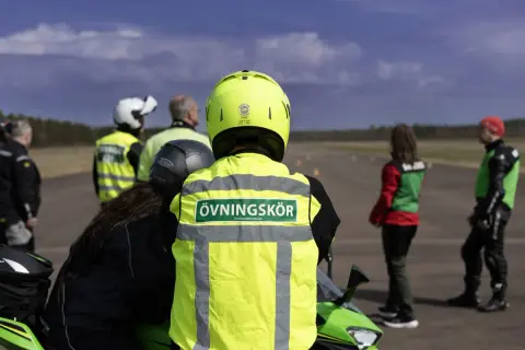 Motorcykelutbildning pågår. En handledare med texten "Övningskör" på västen står redo. Frågan om hur många elever en handledare får ha är relevant för säkerheten.