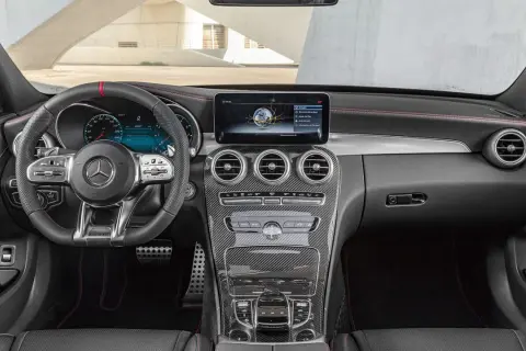 Mercedes C-Klass interior dashboard with steering wheel, infotainment screen, and carbon fiber accents.