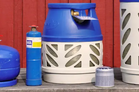 Flera gasflaskor, inklusive en blå gasolflaska och en större vit och blå gasolflaska, står uppradade. Perfekt för din lpg bil.