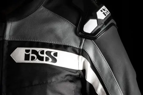 Detaljer på en svart och grå ixs motorcykeljacka med vita logotyper.