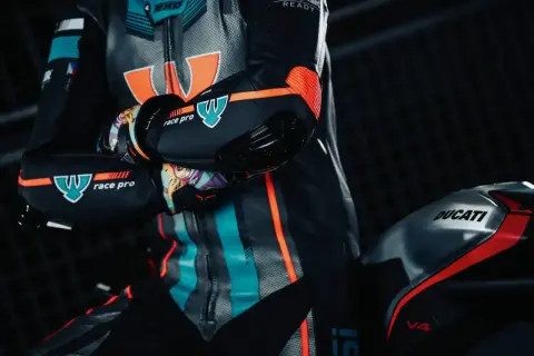 En förare i ett berik skinnställ med orange och turkosa detaljer sitter på en Ducati V4.