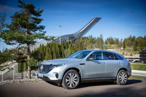 Silver EQC Mercedes står parkerad framför en imponerande hoppbacke i en skogsmiljö.