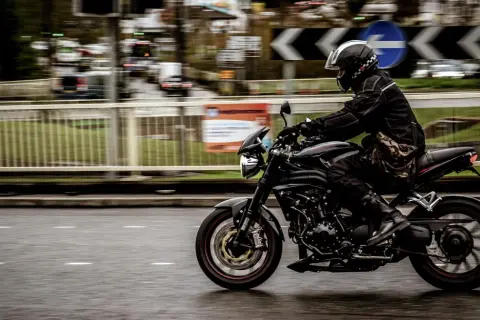 Motorcyklist i full fart på en svart motorcykel, med en praktisk tubhalsduk runt halsen för att skydda mot vinden.