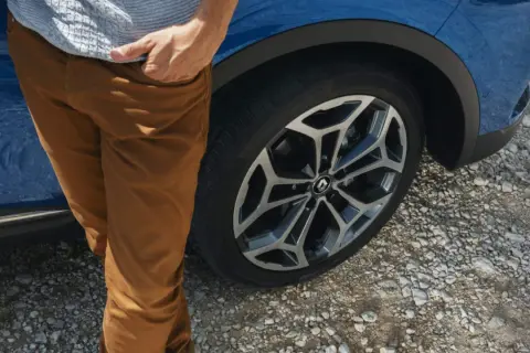 Man med bruna byxor vid en blå Renault Kadjar. Ett hjul syns tydligt, kanske ett tecken på ett Renault Kadjar problem?