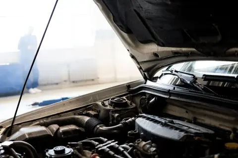 Motorhuven är öppen, visar motordelar. En person står i bakgrunden, kanske redo att byta luftfilter.