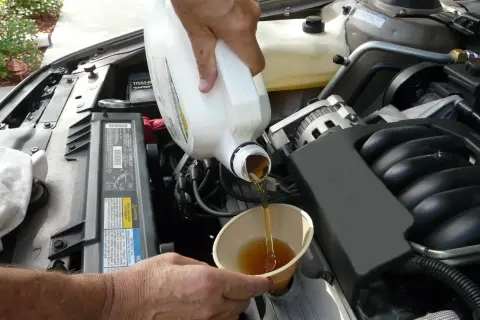 Händer häller ny olja i en bilmotor. För att veta hur ofta byta oljefilter, kolla bilens manual.