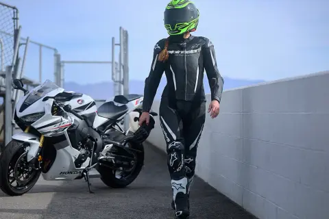 En förare i skinnställ går bredvid en vit Honda. Skinnställ storleksguide hjälper dig hitta rätt passform för din körning.