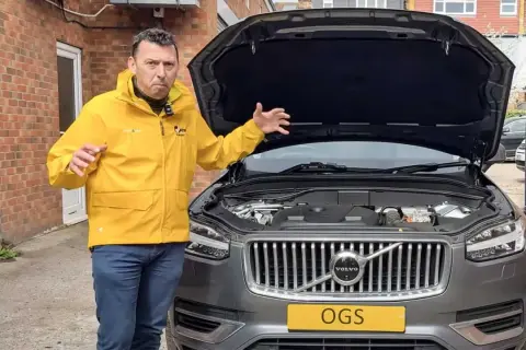 Man i gul jacka gestikulerar vid motorhuven på en Volvo XC60 som inte startar.