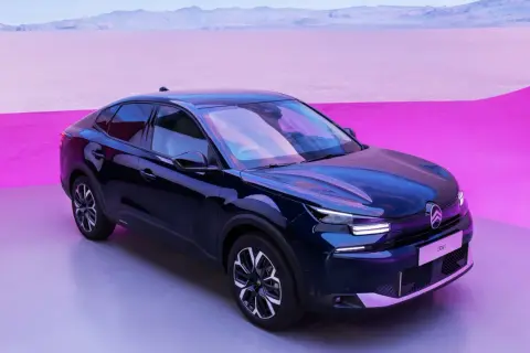 Mörkblå Citroën C4 elbil står på en grå yta med en rosa och lila bakgrund.