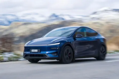 Mörkblå Tesla Model Y Performance kör på en slingrande väg med snöklädda berg i bakgrunden.