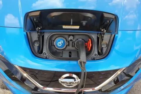 Blue Nissan Leaf with charging port open and cable plugged in.