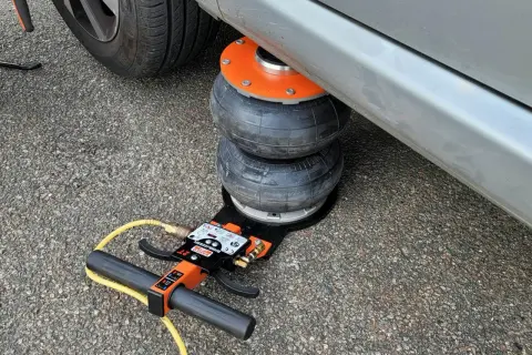 Luftkudde lyfter bilen för däckbyte. En domkraft med slang och handtag syns.