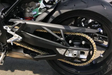 Detaljbild på en motorcykels bakparti med ett gyllene kedjespel mc som löper över ett svart drev. Däcket är ett Michelin.