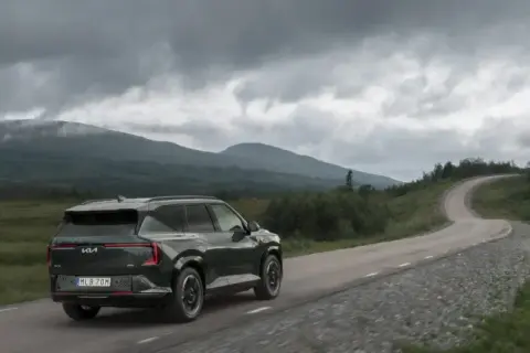 Mörkgrön elbil kör på en slingrande väg genom ett bergigt landskap med molniga himlar. Kanske en försmak av elbilspremie 2026.