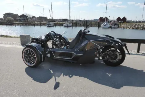 Svart, futuristisk motorcykel på b-kort står vid en hamn med segelbåtar.