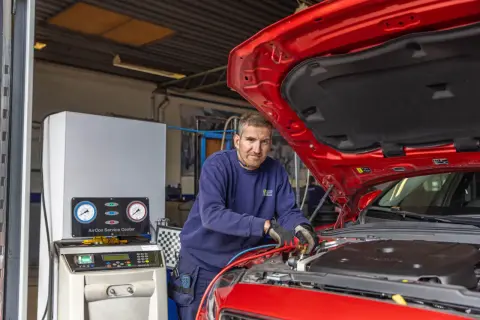 Mekaniker arbetar med bilens AC-system. En maskin med tryckmätare visar hur fungerar ac i bilen.