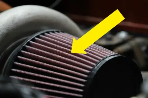 En gul pil pekar på det röda luftfiltermaterialet på ett bilfilter.