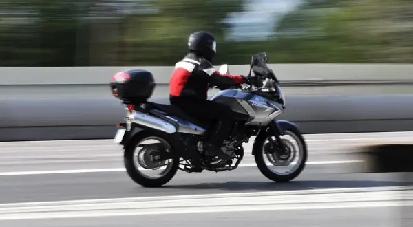 En förare på en pansar mc susar fram på en motorväg, med träd som suddiga gröna streck i bakgrunden.