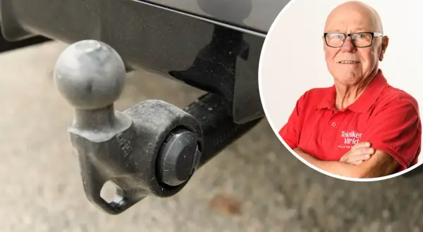 En man i röd tröja från "Tekniker Värld" ler bredvid en avtagbar dragkrok. Viktigt för besiktning.