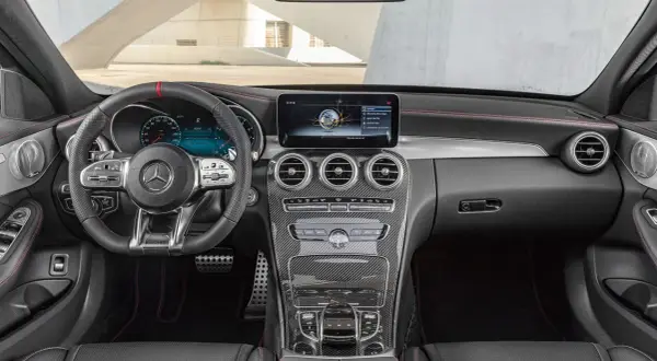 Mercedes C-Klass interior dashboard with steering wheel, infotainment screen, and carbon fiber accents.