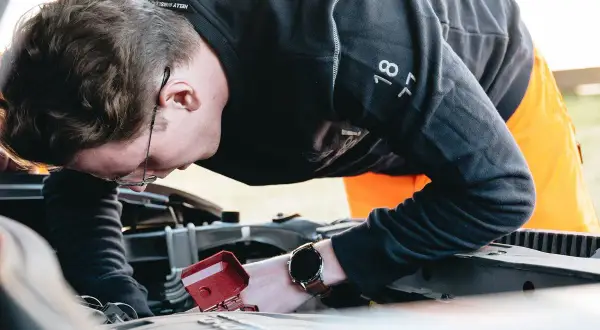 Man med glasögon böjd över bilmotorn, kanske för att fixa det brummande ljudet från bilen.