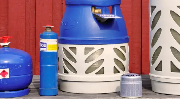 Flera gasflaskor, inklusive en blå gasolflaska och en större vit och blå gasolflaska, står uppradade. Perfekt för din lpg bil.