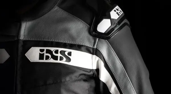 Detaljer på en svart och grå ixs motorcykeljacka med vita logotyper.