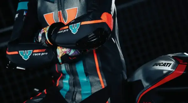 En förare i ett berik skinnställ med orange och turkosa detaljer sitter på en Ducati V4.