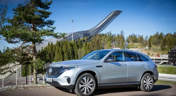 Silver EQC Mercedes står parkerad framför en imponerande hoppbacke i en skogsmiljö.
