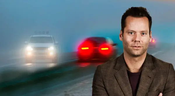 Man i kostym framför dimmig väg med bilar. Viktigt med dimljus regler för säkerhet.