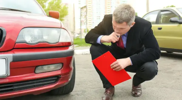 Man i kostym funderar på hur mycket olja rymmer min bil, med en röd pärm i handen vid en röd bil.