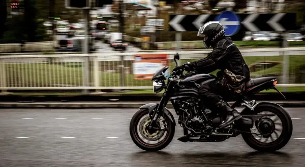 Motorcyklist i full fart på en svart motorcykel, med en praktisk tubhalsduk runt halsen för att skydda mot vinden.