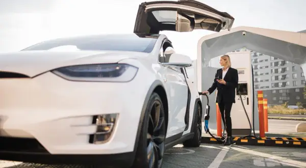 Kvinna laddar elbilen gratis vid laddstation. Bilen har uppfällda dörrar.