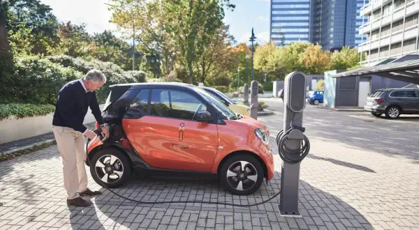 Äldre man kopplar laddkabeln till en orange elbil för att ladda elbil 100 procent.